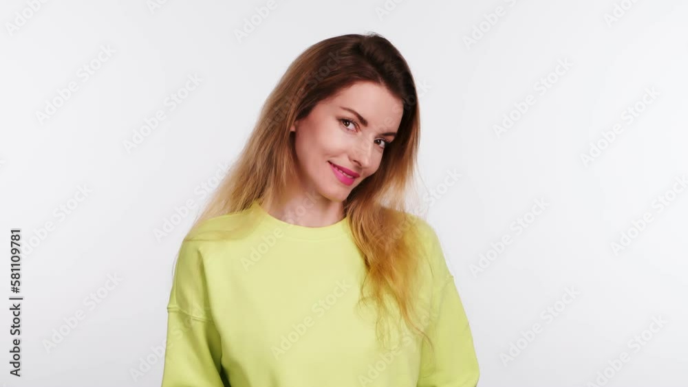 Young woman smiling shy looking at camera. Happy positive emotional blonde girl, long hair. Joyful cheerful pretty lady in yellow sweatshirt, smile face. Indoors studio, isolated on white background Young woman smiling shy looking at camera. Happy positive emotional blonde girl, long hair. Joyful cheerful pretty lady in yellow sweatshirt, smile face. Indoors studio, isolated on white background