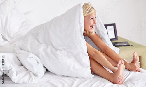 Bring on the day. a smiling woman covered in a duvet lying on her bed.