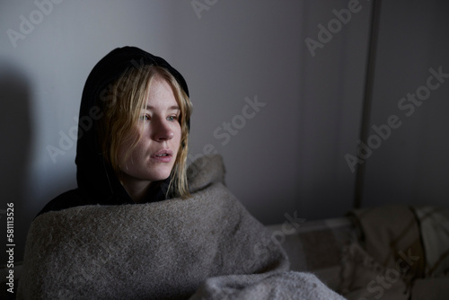 Teenage girl sitting on sofa wrapped in blanket