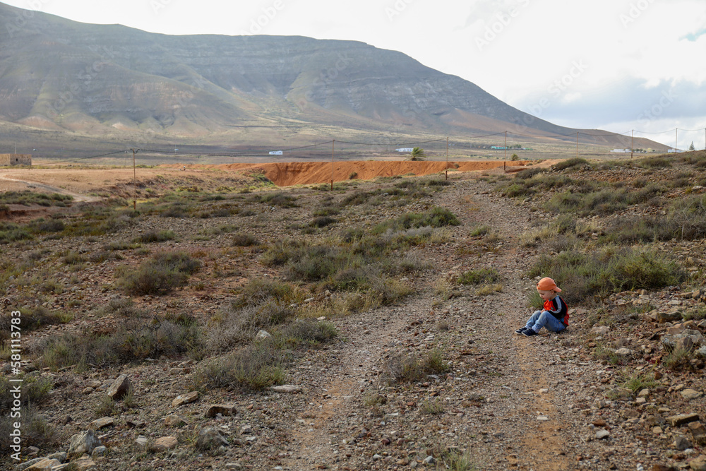 Caucasian child sitting on the edge of a path in a desert area.