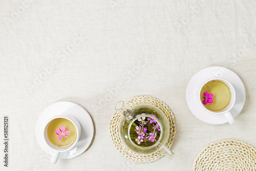 Fireweed tea in white cups and transparent glass teapot, herbal hot tea from green leaves of ivan chai on textile tablecloth. Top view healthy drink and wild flowering willow-herb, tea time