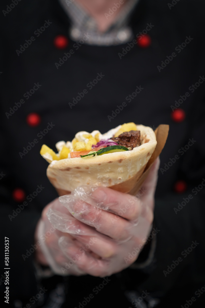 Cook holds fresh gyros in hands. Chef cooked traditional Greek fast food dish for lunch. Pita bread stuffed with grilled chicken meat, fries and tzatziki sauce