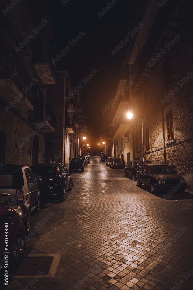 Typical italian street with parked cars at night.