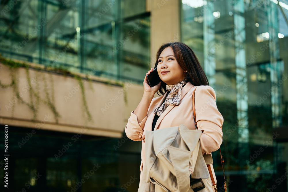 Fototapeta premium Smiling Asian businesswoman communicating on cell phone while walking on street.