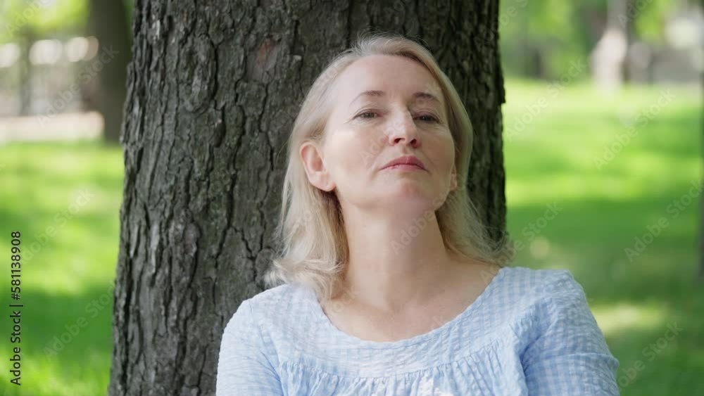 Thoughtful mature woman sitting under tree in park, almost crying, sadness Thoughtful mature woman sitting under tree in park, almost crying, sadness