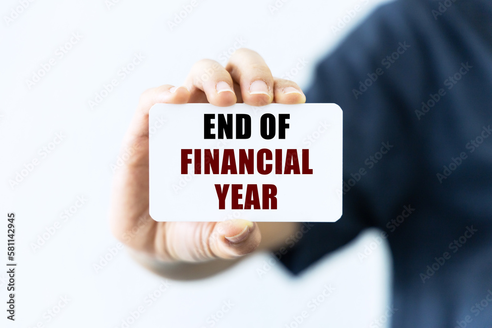 End of financial year text on blank business card being held by a woman's hand with blurred background. Business concept about end financial period. End of financial year text on blank business card being held by a woman's hand with blurred background. Business concept about end financial period.