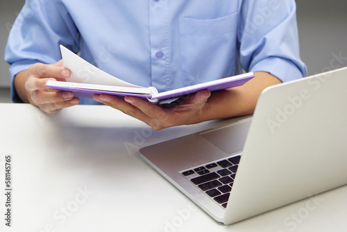 Close up hand of businessperson are opening a read book and laptop in front. Concept of business and data validation.