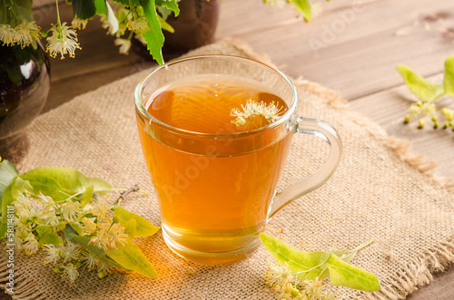Healing herbal tea with lime blossom in a mug on a dark wooden table with flowers
