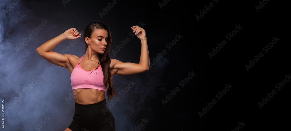 Fototapeta premium Beautiful fitness girl. Woman in shorts and pink sportswear. Black background with smoke. A high resolution. Photo for advertising