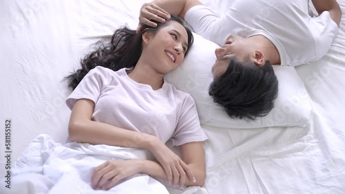 Happy asian couple lying in bed and smiling at each other on holiday morning.