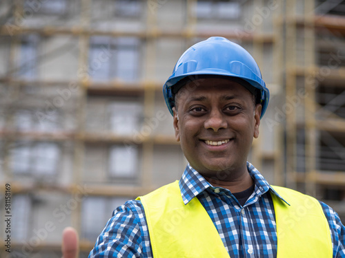 Portrait of a smiling Indian civil engineer or factory worker wearing a blue helmet and looking at camera