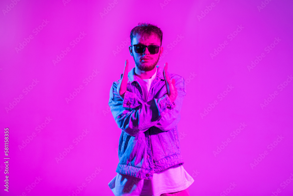 Stylish fashion dancer man in trendy denim clothes with sunglasses is dancing in a creative color studio with pink and neon lights Stylish fashion dancer man in trendy denim clothes with sunglasses is dancing in a creative color studio with pink and neon lights