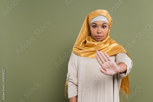 Multiracial woman in hijab showing stop gesture isolated on green. © LIGHTFIELD STUDIOS