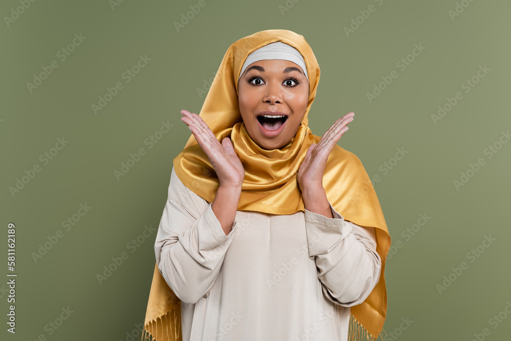 Astonished multiracial woman in hijab looking at camera isolated on green. Astonished multiracial woman in hijab looking at camera isolated on green.