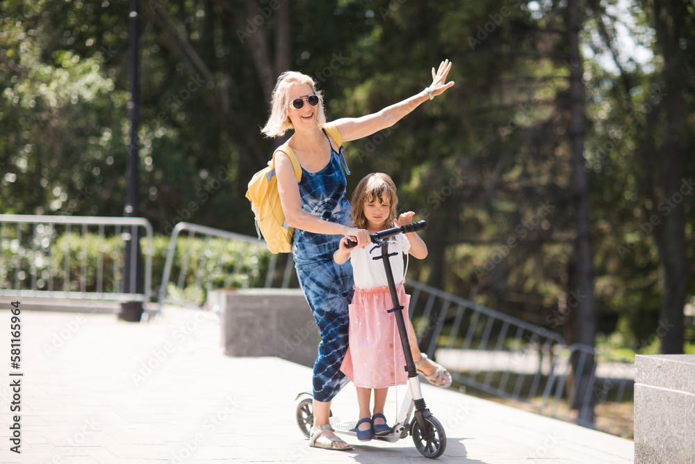 mom and child daughter ride a scooter in the park in summer. happy family has fun together in nature mom and child daughter ride a scooter in the park in summer. happy family has fun together in nature