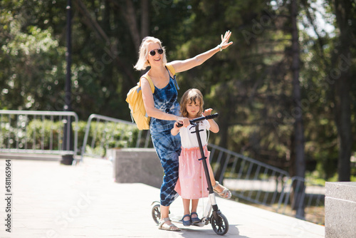 mom and child daughter ride a scooter in the park in summer. happy family has fun together in nature