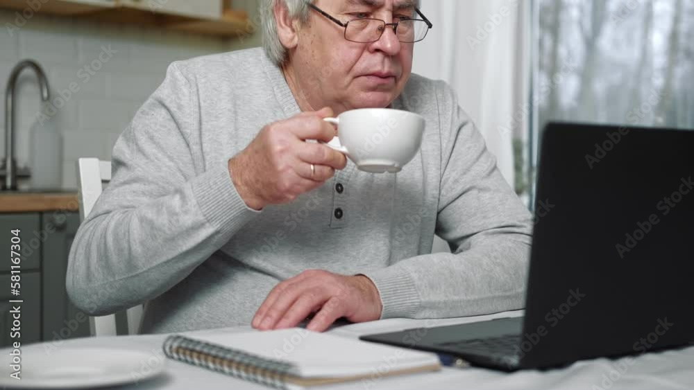 Senior male business owner in glasses sitting at desk in front of laptop. Successful older male working at home. Grey haired 60s - 70s Aged busy man typing keyboard, drinking coffee. Distance office Senior male business owner in glasses sitting at desk in front of laptop. Successful older male working at home. Grey haired 60s - 70s Aged busy man typing keyboard, drinking coffee. Distance office