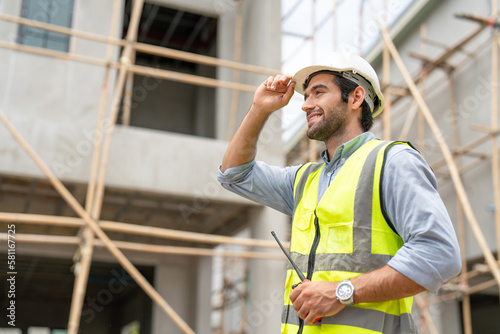 Portrait of male civil engineer wear safety vest with white helmet holding walkie talkie walking to inspection housing estate at construction site photo