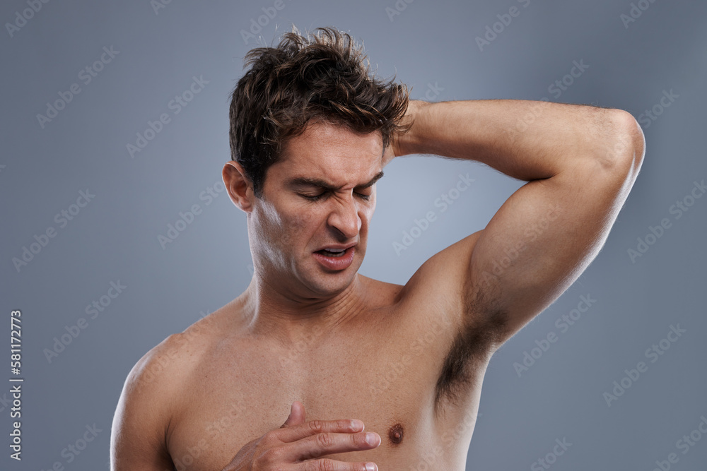 I smell expired. a handsome young man grimacing while smelling his armpit.