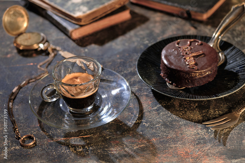an freshly made espresso cup next to a fancy chocolate tart , books and a poket watch are in the background photo
