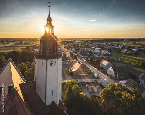 wieża kościoła z blaskiem zachodzącego słońca z promieniami i widokiem wsi opolskiej w Polsce