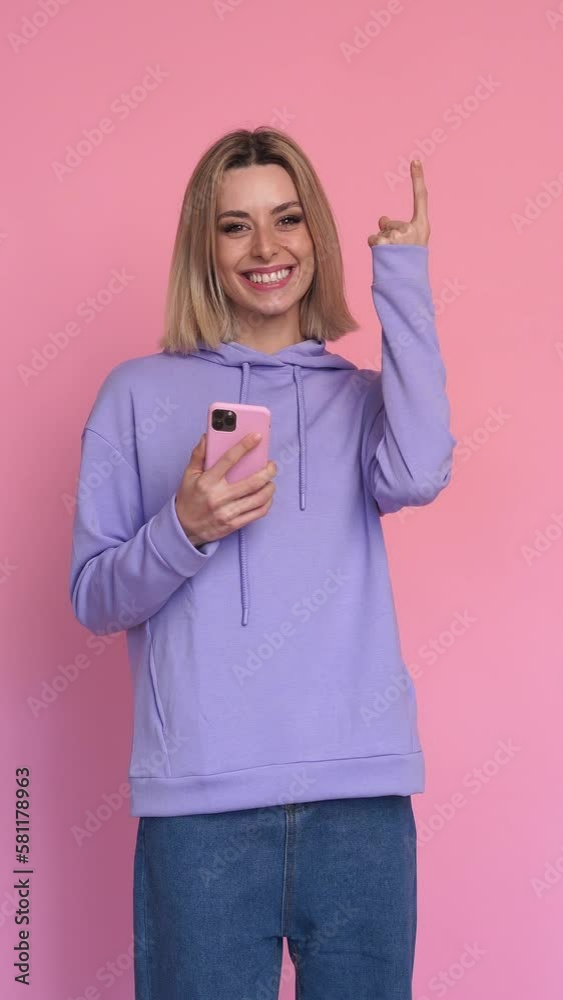 Cheerful woman with smartphone pointing aside. Vertical video. Cheerful woman with smartphone pointing aside. Vertical video.