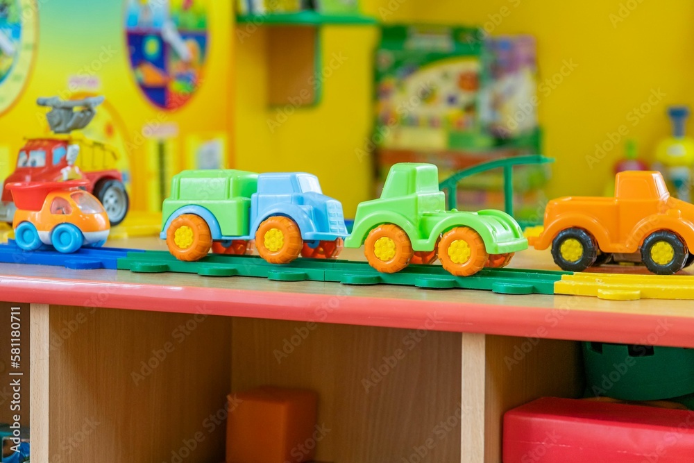 Several plastic toy multi-colored cars stand on wooden table against blurred color background.
