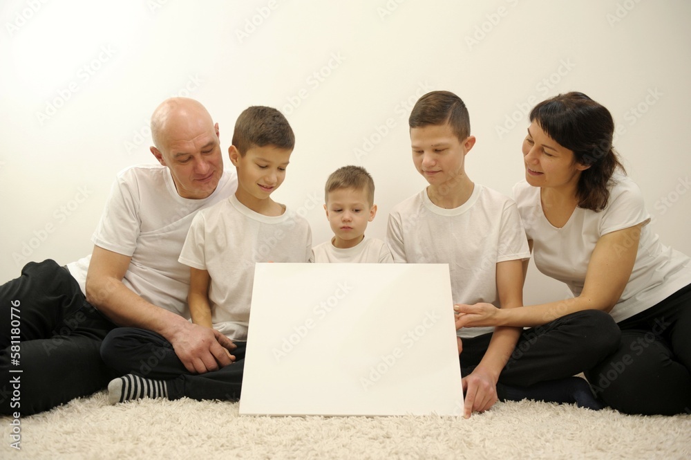 family with white board, pointing or presenting empty white placard family of five holding paper poster you can write your ad on it they look at the banner and smile at them white t-shirts family with white board, pointing or presenting empty white placard family of five holding paper poster you can write your ad on it they look at the banner and smile at them white t-shirts