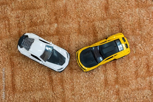Two toy models of sports cars stand on tufted brown carpet. View from above.