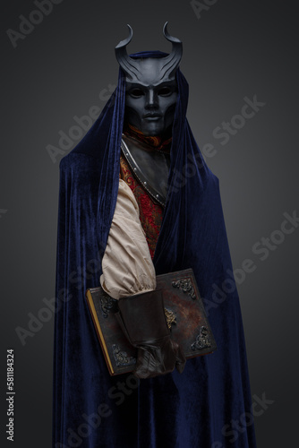 Shot of cultist with horned mask and dark blue cape against gray background.