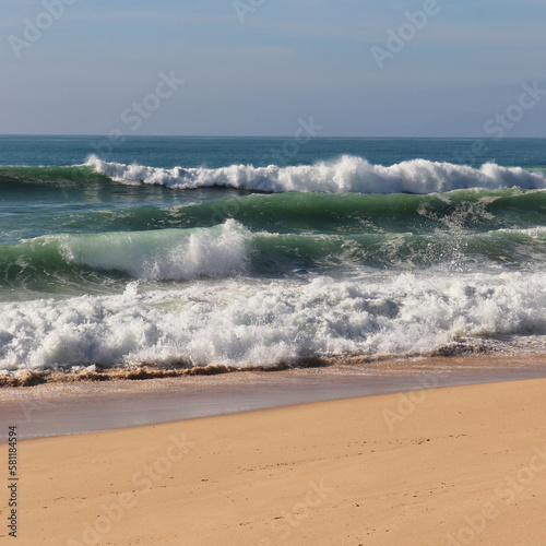Waves in the Atlantic Ocean crashing into the sandy beach on a sunny winter day near Lisbon, Portugal.