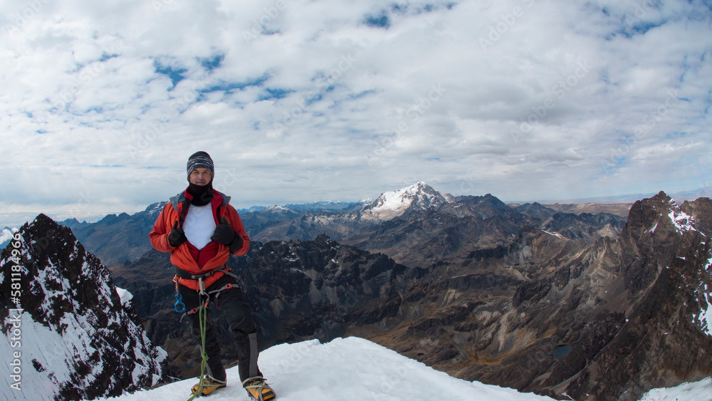 Young male climber standing on the summit of snowy mountain wearing helmet, headlamp, red coat and rope