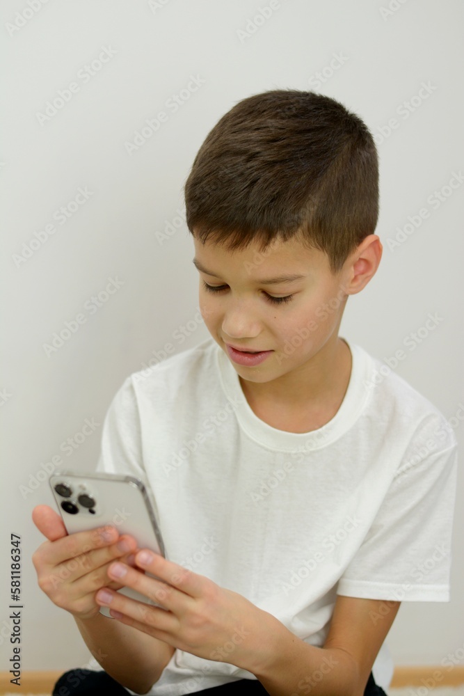 a boy in a large oversized T-shirt sits in mobile phone plays games joy of social networking mobile applications on a white background teenager long fingers 10 -14 years old a boy in a large oversized T-shirt sits in mobile phone plays games joy of social networking mobile applications on a white background teenager long fingers 10 -14 years old