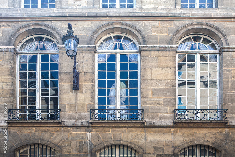 Paris ancient stone building facade with three rows of French windows, stucco fretwork, small wrought iron balconies and wall lamp.