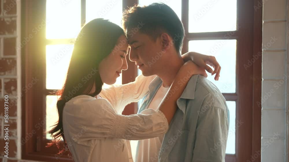 Asian young couple embracing while standing by the window. Asian young couple embracing while standing by the window.
