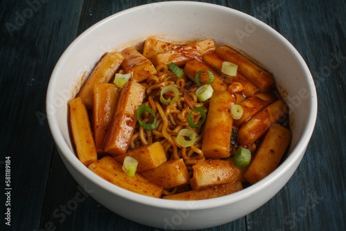 Rapokki or rabokki stand for ramyeon and teokpokki, a korean rice cake mix with instan noodles garnish with sesame seed and cut chives. Isolated in dark blue background