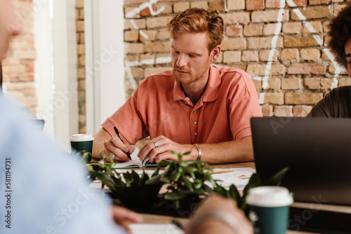 Man writing down notes while working in office with his colleagues