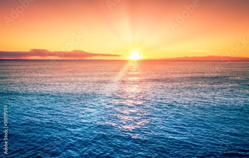 Beautiful orange sunset with sun rays, blue ocean water, calm weather sunny day.