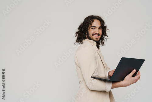 Cheerful hispanic man working on laptop isolated over white wall