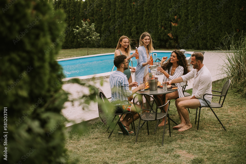 Group of young people cheering with cider by the pool in the garden