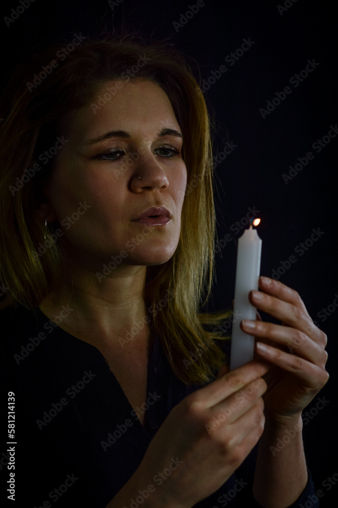 Obraz premium portrait of a beautiful blonde woman blowing out the flame of a candle she is holding