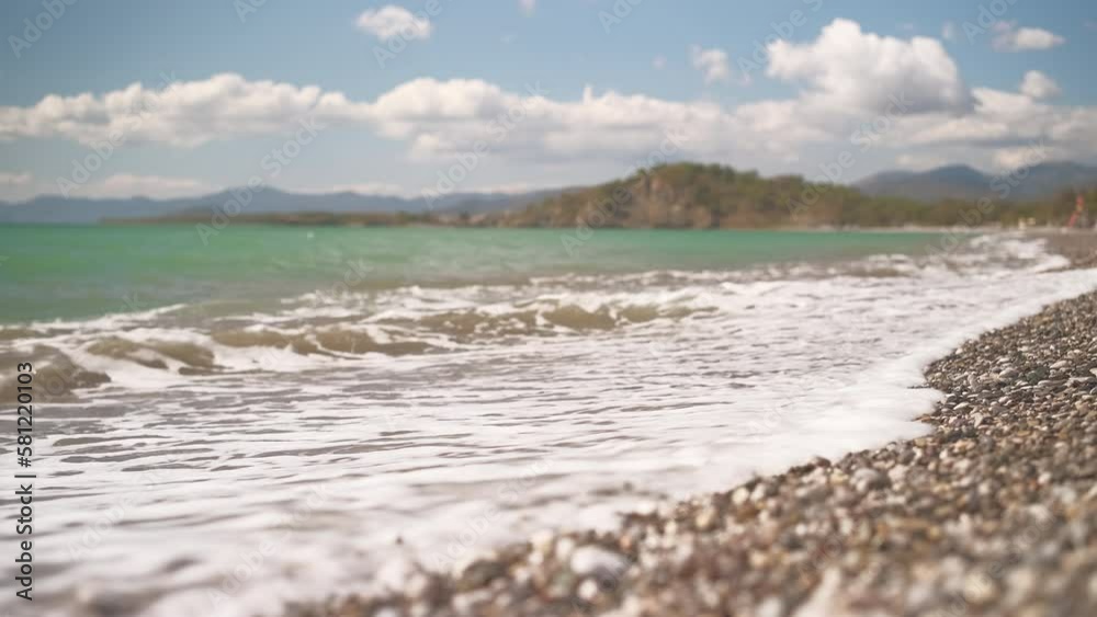 View of the bay on a pebble beach in the Aegean Sea, 4k live video, legs of a man in the frame passing to the sea, selective focus, beautiful sea waves washing the beach, vacation time View of the bay on a pebble beach in the Aegean Sea, 4k live video, legs of a man in the frame passing to the sea, selective focus, beautiful sea waves washing the beach, vacation time