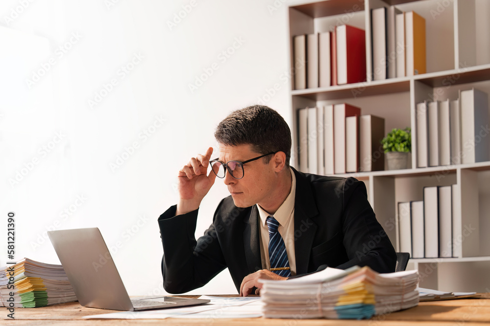 Portrait of businessman inside office with laptop, businessman in glasses and business suit sitting working in the office Portrait of businessman inside office with laptop, businessman in glasses and business suit sitting working in the office