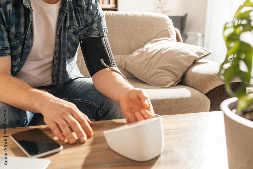 Close-up of a man's hands measuring his blood pressure with a special cuff and tonometer. Health check at home. Problems of hypotension and hypertension. Close-up of a man's hands measuring his blood pressure with a special cuff and tonometer. Health check at home. Problems of hypotension and hypertension.