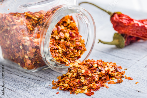 Dry chili pepper flakes. Crushed red peppers in jar on white table.