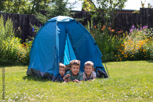 Three little boys lie in a blue tourist tent in the yard.