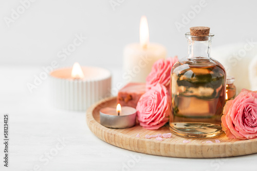 Aromatherapy. Concept of pure organic essential rose oil. Elixir with plant based floral or herbal ingredients. Pink flowers extract. Spa atmosphere with candle, towel. White background