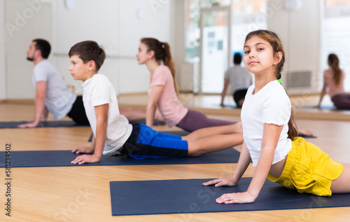 Girl looking at camera while doing cobra pose with her brother and parents on yoga family training.