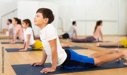 Positive sporty boy enjoying yoga class with teen sister and parents in fitness studio, doing stretching asana Bhujangasana