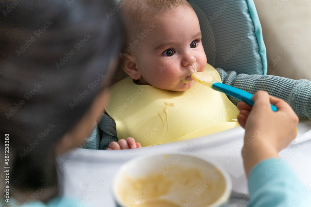 Close-up of an unrecognizable adult feeding porridge to a baby sitting in a highchair Close-up of an unrecognizable adult feeding porridge to a baby sitting in a highchair